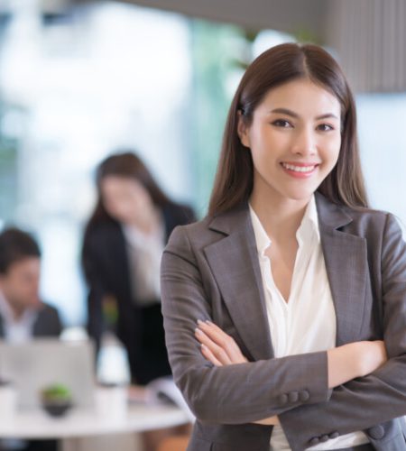 Portrait of successful young Asian businesswoman at office, colleagues in background.